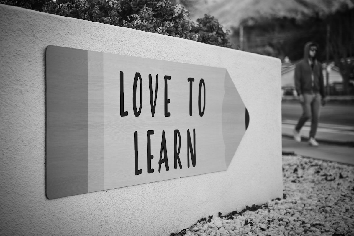 A man walks on the sidewalk past a sign shaped like a pencil that says "Love To Learn"